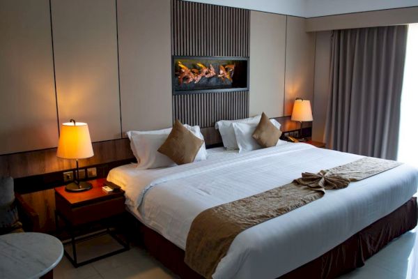 The image shows a neatly made hotel room with a large bed, bedside lamps, and a decorative wall feature, creating a cozy atmosphere.