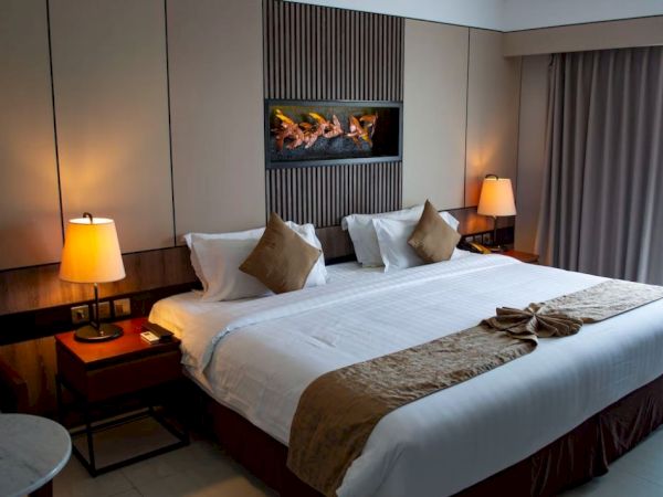 The image shows a neatly made hotel room with a large bed, bedside lamps, and a decorative wall feature, creating a cozy atmosphere.