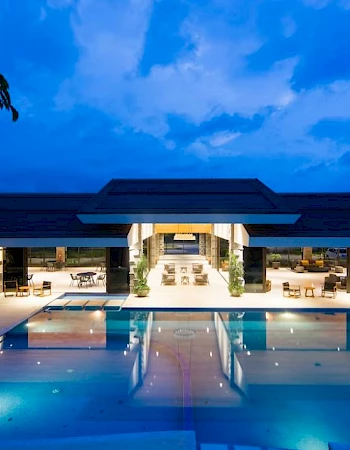 Modern building with a large outdoor swimming pool, set against a blue evening sky.