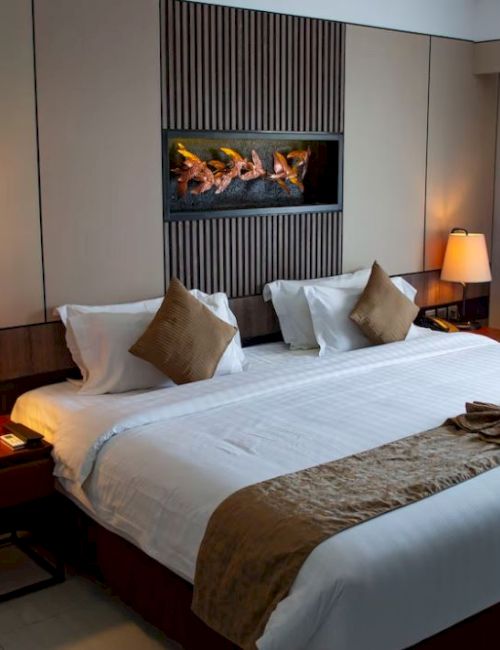 A well-decorated hotel room features a large bed with brown accents, two bedside tables with lamps, and a modern wall artwork.