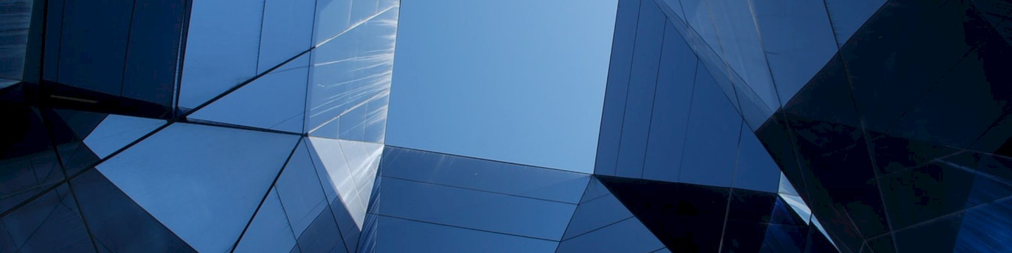 Abstract view of a modern glass building, with reflective surfaces and a clear blue sky visible through a geometric opening.