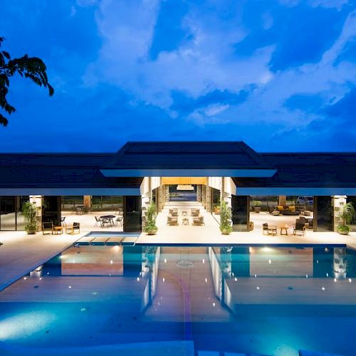 A luxurious, modern building with a large, illuminated swimming pool in front, set against an evening sky backdrop.