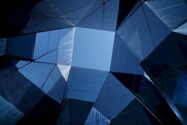 Abstract architectural design with reflective glass panels forming a geometric structure against a blue sky.