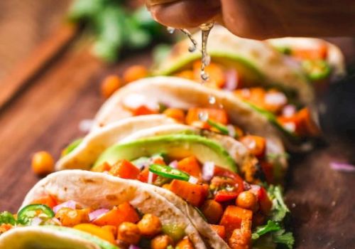 Tacos filled with chickpeas, avocado, and vegetables on a wooden board, with lime being squeezed over them.