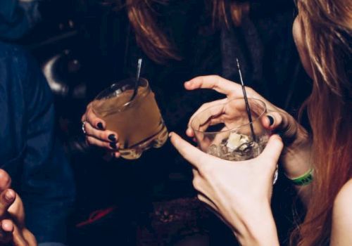 People are enjoying a night out, holding drinks, and engaging in conversation, amid a lively atmosphere.