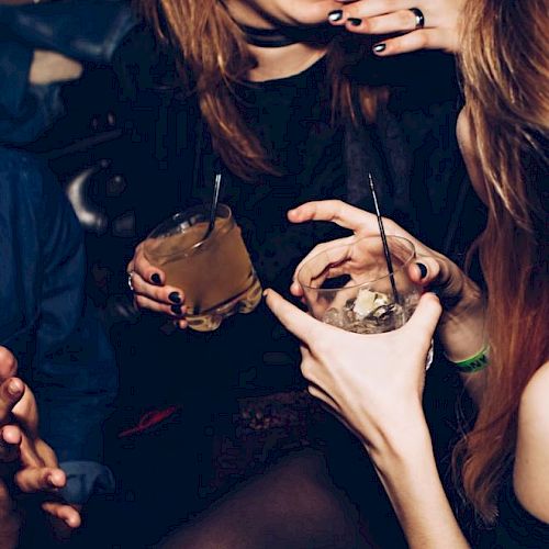 People are enjoying a night out, holding drinks, and engaging in conversation, amid a lively atmosphere.