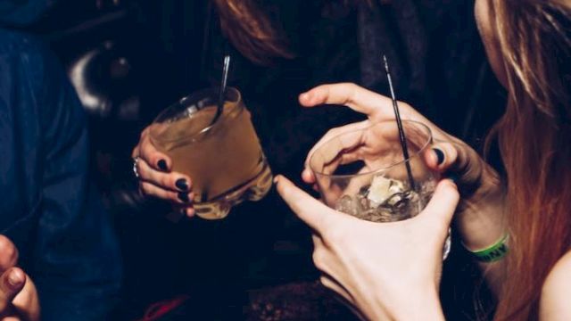 People are enjoying a night out, holding drinks, and engaging in conversation, amid a lively atmosphere.