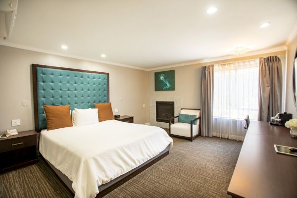 A modern hotel room with a large bed, teal headboard, desk, chair, and window with curtains, providing a comfortable and elegant atmosphere.