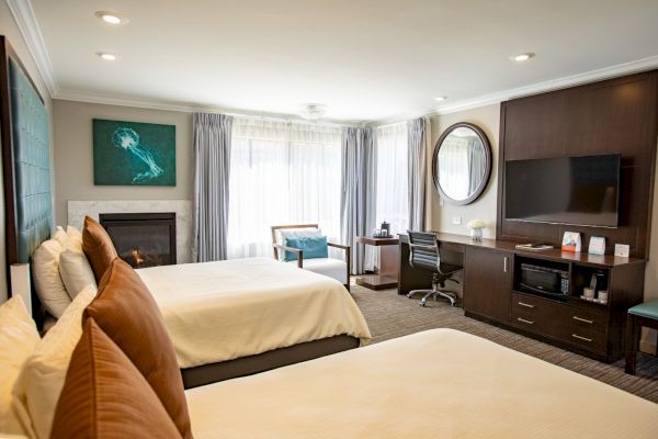 A hotel room with two beds, a TV, a desk, a mirror, a fireplace, and a seating area by the window.