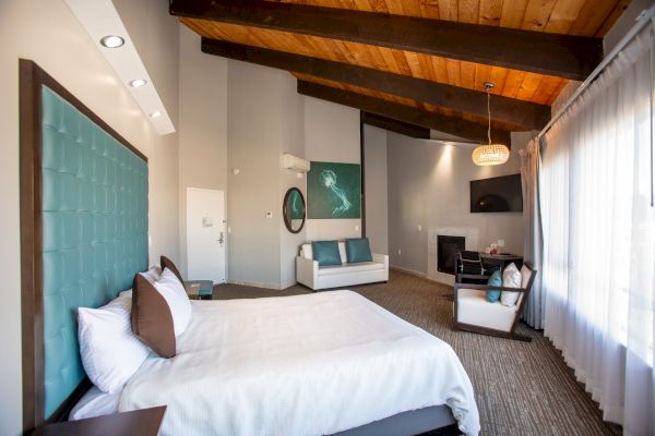 A modern bedroom with a high ceiling, featuring a bed, couch, artwork, and large window allowing natural light.