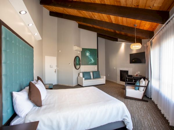 A modern bedroom with a high ceiling, featuring a bed, couch, artwork, and large window allowing natural light.