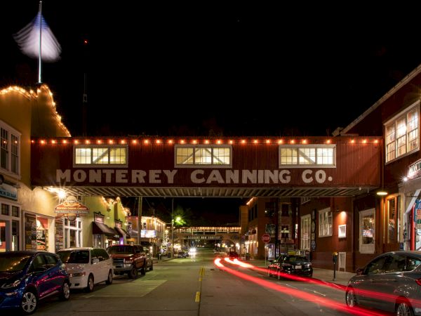 A night scene of a street with the "Monterey Canning Co." bridge, cars, and lit buildings, showing light trails from moving vehicles.