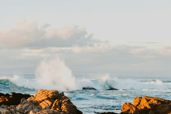 A rocky shoreline with waves crashing against the rocks under a partly cloudy sky during sunset or sunrise.