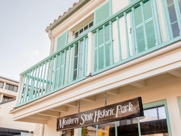A building with mint green shutters and balcony, with a sign reading "Monterey State Historic Park" hanging below the balcony.