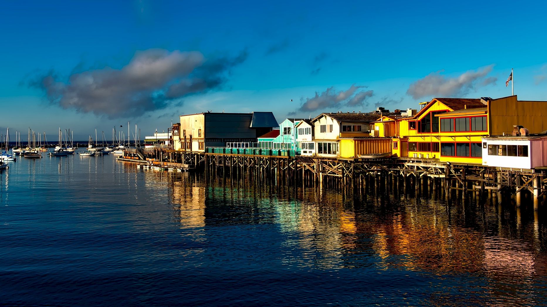 A vibrant waterfront scene with colorful buildings and sailboats docked at a marina under a clear blue sky.