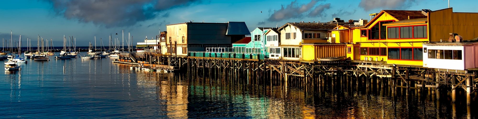 A vibrant waterfront scene with colorful buildings and sailboats docked at a marina under a clear blue sky.