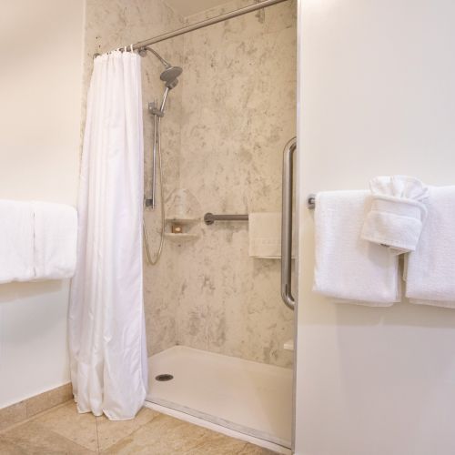 The image shows a bathroom with a shower, white towels on bars, a shower curtain, and a marble-like wall. The floor is tiled.