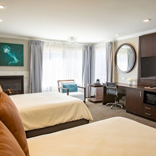 A hotel room with two beds, a fireplace, desk, TV, large window, and modern decor, creating a cozy and inviting atmosphere.