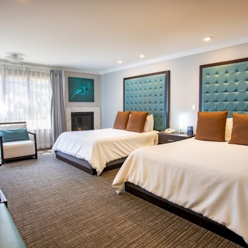 A hotel room with two double beds, teal headboards, a desk, chair, and a window with curtains, creating a cozy and modern atmosphere.