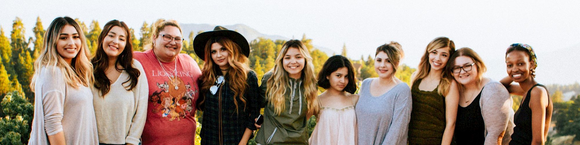 A group of ten people stand outdoors, smiling, in casual clothing, with natural scenery in the background.