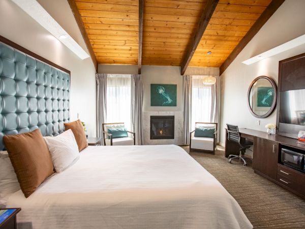 A cozy hotel room with a vaulted wooden ceiling, bed, chairs, fireplace, desk, TV, and art on the walls, creating a warm ambiance.
