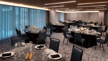 The image shows an elegantly set banquet room with round tables, chairs, tableware, and candles, ready for an event or gathering.