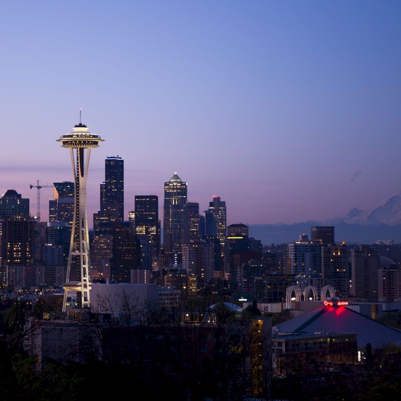 Seattle skyline at dusk with Space Needle, city buildings, and Mount Rainier in the background, under a clear twilight sky.