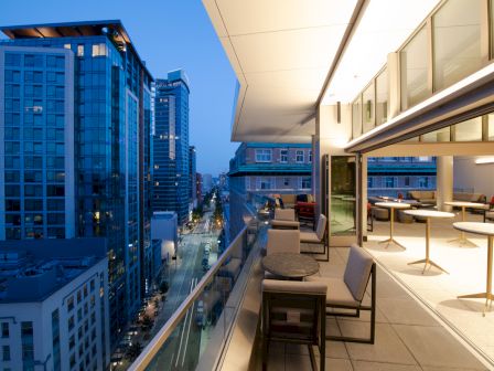 A modern rooftop terrace with outdoor seating overlooks a cityscape of tall buildings and lit streets at dusk.