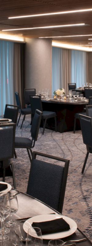 The image shows an elegantly set dining area with round tables, chairs, glassware, and folded napkins, creating a sophisticated ambiance.