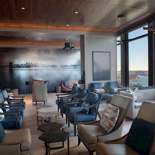 A modern lounge with comfortable seating, large windows overlooking water and a Ferris wheel, and a mural on the back wall.