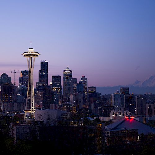 Seattle skyline at dusk with the Space Needle prominently featured against the cityscape and Mount Rainier in the background.