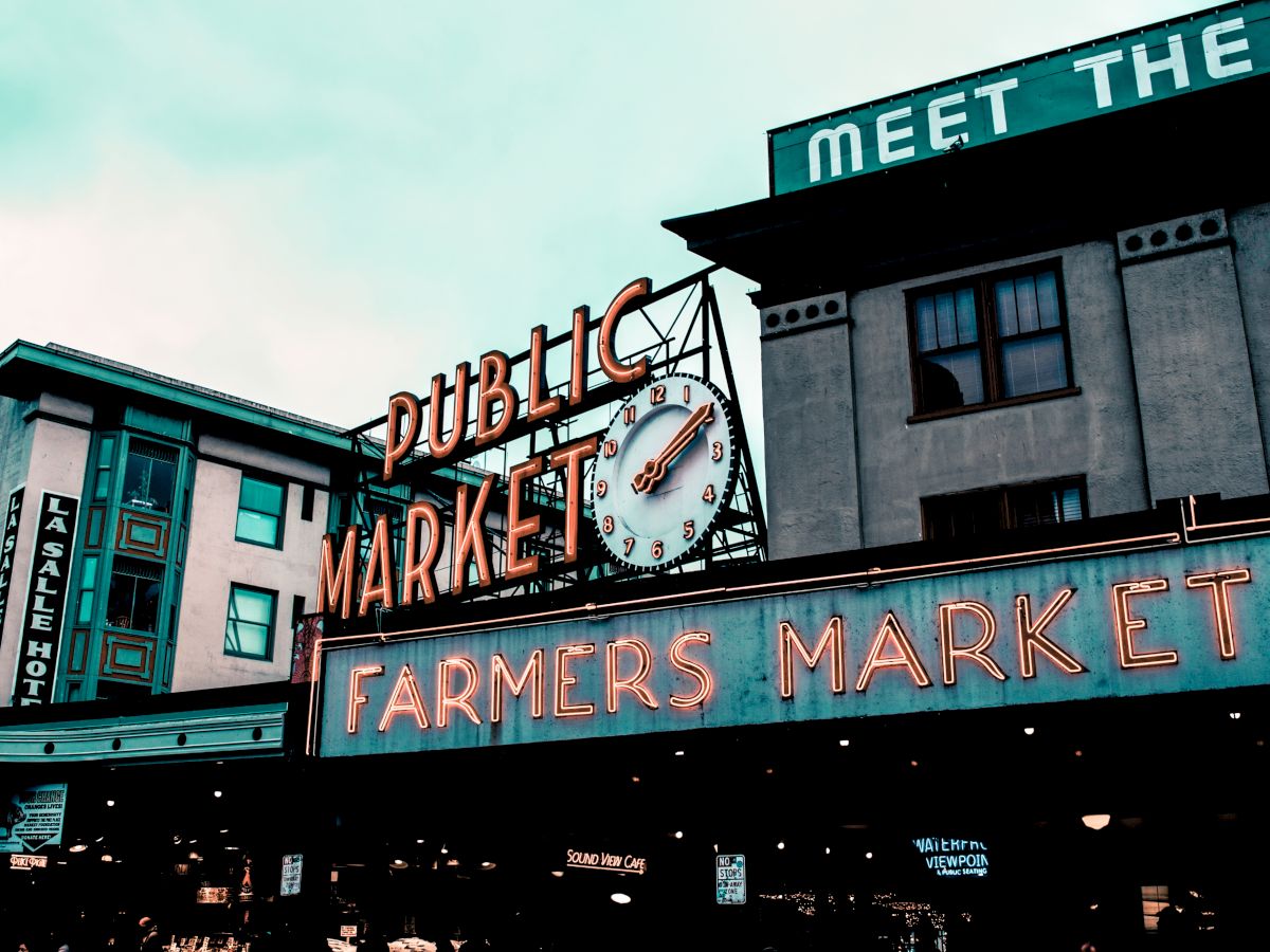 The image shows a farmers market with a neon sign reading "Public Market" and "Farmers Market" under a vintage clock.