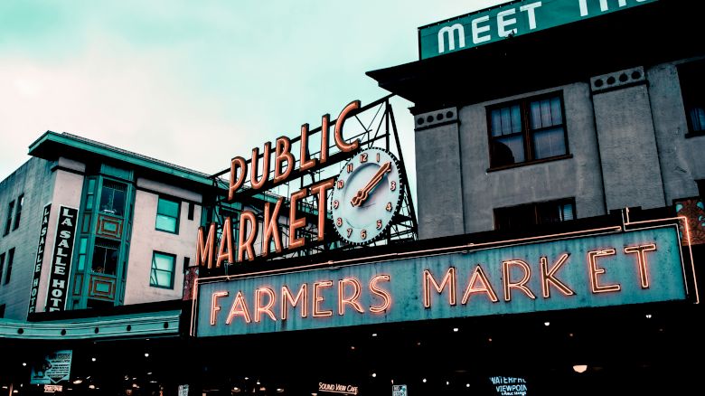 The image shows a farmers market with a neon sign reading "Public Market" and "Farmers Market" under a vintage clock.